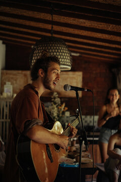 Young man musician plays the guitar and sings into a microphone.