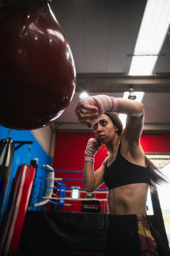 Fit female boxer punching ball wearing straps on wrist in gym