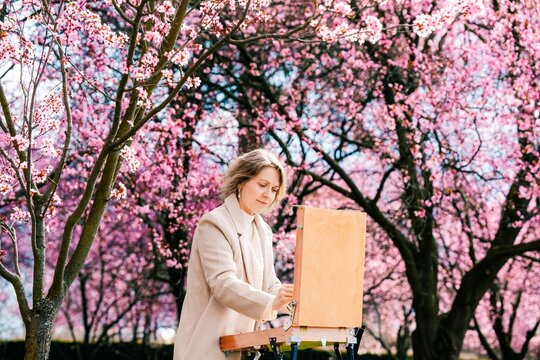 Woman painting a picture of coffee in a blooming rose garden