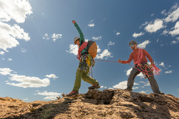 Two people are climbing a mountain, one of them is wearing a green jacket. The other person is...