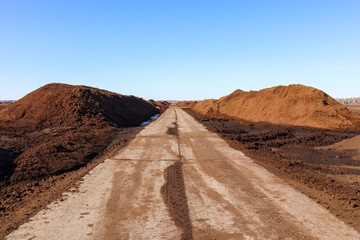 Straight long concrete path through a peat bog with large peat hills and blue sky in the background