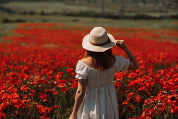 Field of poppies woman. Happy woman in a wight dress and hat stand through a blooming field of...