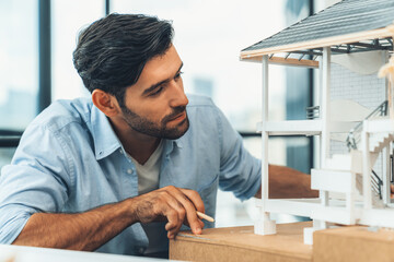 Closeup portrait of smart caucasian architect engineer inspect house model while thinking about...