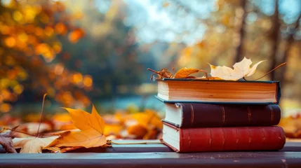 Fototapeten A stack of books in various colors placed neatly on top of a wooden table surrounded by autumn leaves © tashechka