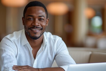 With a laptop open before him, a cheerful African-American entrepreneur smiles warmly, engaging with the camera