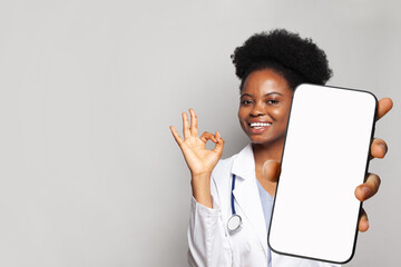 Happy doctor shows a phone with a blank display. Online medical consultation and medical healthcare and application. - obrazy, fototapety, plakaty