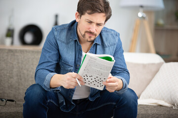 young man sitting on sofa and doing crossword puzzle