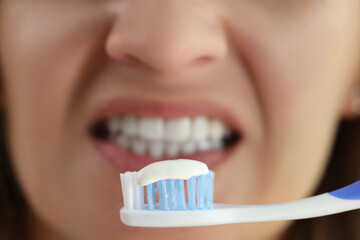Toothpaste on toothbrush in front of woman's face with white teeth close-up.