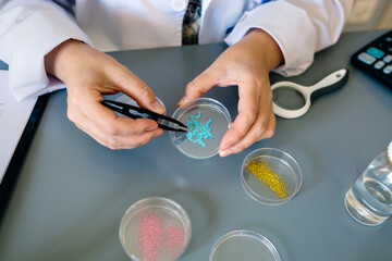 Unrecognizable female chemist technician examining blue glitter in facial cream sample over petri dish on environment research laboratory. Scientist studying microplastics on cosmetic composition.