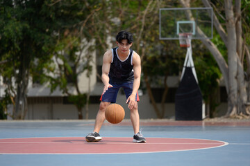 Obraz premium Young muscular basketball player dribbling a ball on an outdoor court