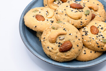 Isolated Blue Plate filled with Healthy Whole Grain Cookies with different seeds, cashew nuts, almond, black sesame, pumpkin seed on white background