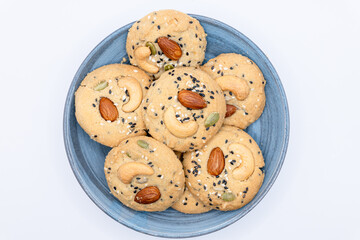 Isolated Blue Plate filled with Healthy Whole Grain Cookies with different seeds, cashew nuts, almond, black sesame, pumpkin seed on white background
