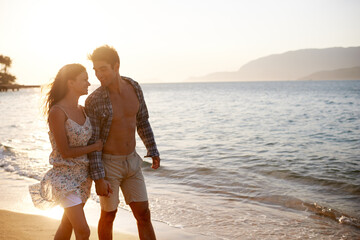 Love, waves and happy couple walking at ocean for tropical holiday adventure, relax and bonding together. Nature, man and woman on romantic date with beach, sunset sky and connection on vacation.
