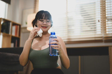 Happy young woman drinking water after training while sitting on exercise mat at home