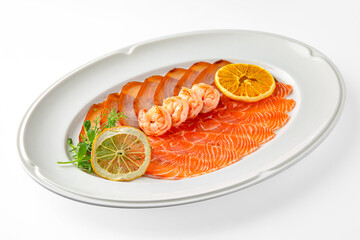 Sliced delicacy fish: salmon and butter fish and shrimp on a white plate. Banquet festive dishes. Gourmet restaurant menu. White background.