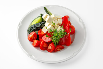 Snack of fresh vegetables: tomatoes, cucumbers, sweet peppers and cheese on a white plate. Banquet festive dishes. Gourmet restaurant menu. White background.