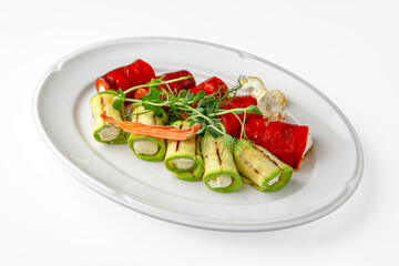 Zucchini and sweet pepper rolls with cheese on a white plate. Banquet festive dishes. Gourmet restaurant menu. White background.