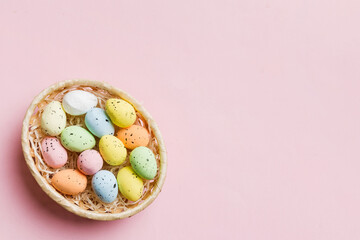 Colorful Easter eggs in wicker basket against colored background, closeup. top view with copy space