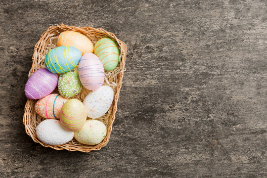 Colorful Easter eggs in wicker basket against colored background, closeup. top view with copy space