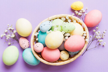 Happy Easter composition. Easter eggs in basket on colored table with gypsophila. Natural dyed colorful eggs background top view with copy space