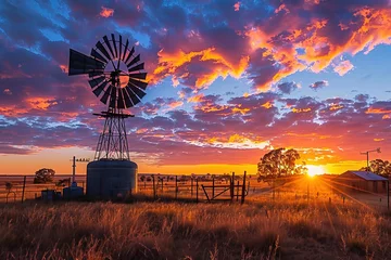 Fotobehang Colorful Australian outback sunset landscape with a windmill, water tank and gumtrees and a firey sky with clouds with a sunburst. © Inge
