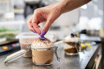 A skilled chef delicately garnishes a gourmet dessert with a purple flower, showcasing culinary artistry