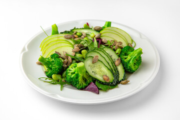 Vegetarian low-calorie salad of green vegetables, fruits and seeds on a white plate. Banquet festive dishes. Gourmet restaurant menu. White background.