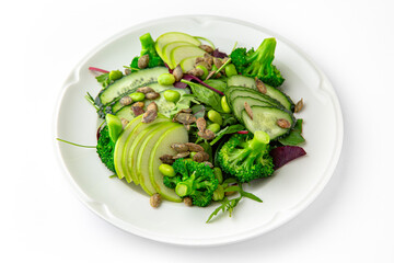 Vegetarian low-calorie salad of green vegetables, fruits and seeds on a white plate. Banquet festive dishes. Gourmet restaurant menu. White background.