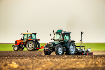 Two tractors plough and sow in tandem on a vast farm field