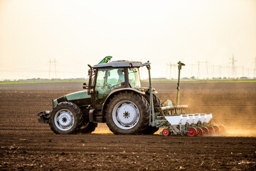 Modern tractor seeding, planting agricultural field at dusk