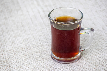 Black tea or red tea in a glass cup on white textured background. In Bangladesh, this is called Rong Cha or Lal Cha. 