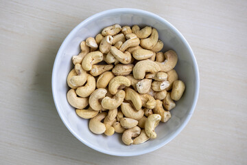 Healthy cashew nuts in a white bowl on a wooden background. Its scientific name is Anacardium occidentale and In the Bengali language, it is called Kaju Badam. Top view. 