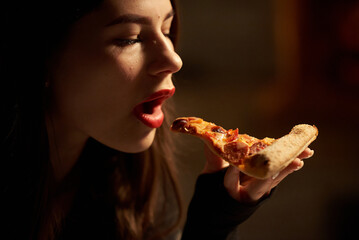 Beautiful girl with red lipstick eats pepperoni pizza in a pizzeria
