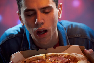 A young guy student sniffs fresh paperoni pizza in a cardboard box