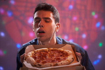 A young guy enjoys the smell of delicious pizza in a cardboard box