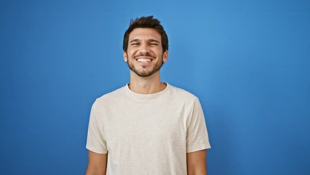 Handsome hispanic man with beard smiling and looking up against a blue wall outdoors.