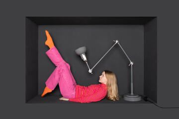 Teenage girl lying in front of electric lamp by black background
