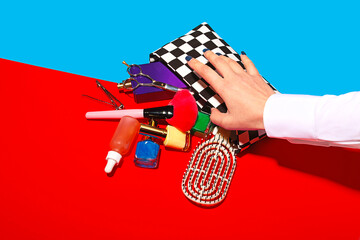 Studio shot of female hand touching cosmetics falling out of checked purse