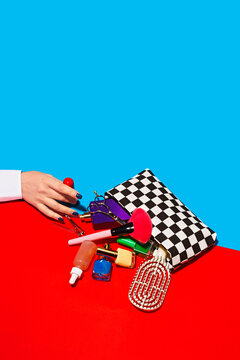 Studio shot of female hand touching cosmetics falling out of checked purse