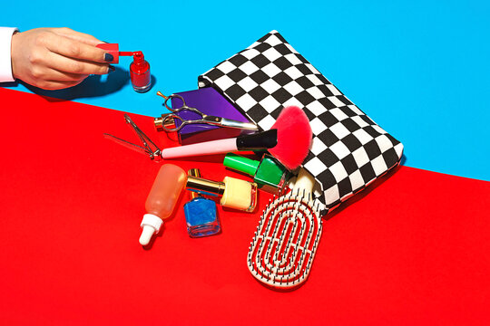 Studio shot of female hand touching cosmetics falling out of checked purse