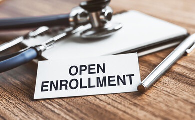 The text open enrollment is written on notepad near a stethoscope on a wooden background. Medical...