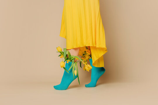 Woman wearing yellow skirt with tulips in blue socks against beige background
