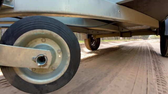Trailer wheels rotation on sandy road. Car driving for cargo delivery. Bottom view, camera mounted beneath car chassis. Wheel rotation, spinning tyres. Freight Transporting using lightweight