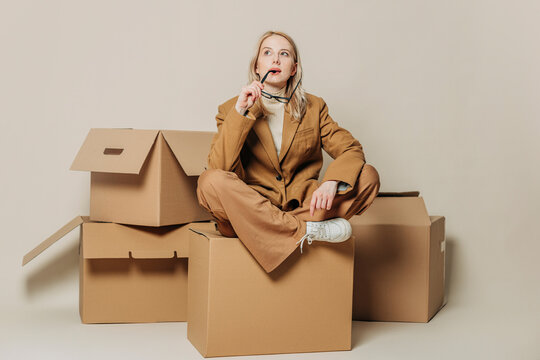 Thoughtful businesswoman sitting on cardboard box against white background