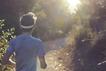 Fotobehang athlete in a sweatband jogging on a sunlit trail © primopiano