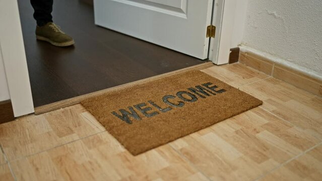 Brown doormat with 'welcome' text inside home entryway, with wooden floor and white door.