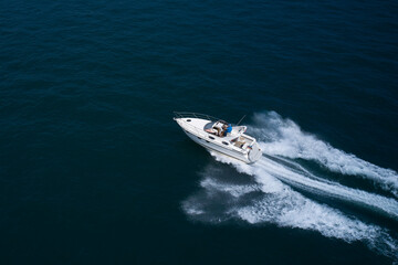 A large modern high-speed White boat with a man on board moves quickly on dark blue water, aerial view. Large speed boat moving on dark blue water top view.