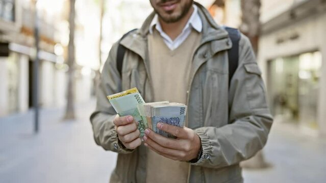 A young hispanic man examines foreign currency on a city street, symbolizing urban finance and travel.