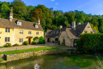 Fototapeta na wymiar Scenic view of traditional old cottage houses and a street by a river in a beautiful English village, Castle Combe village in the Cotswolds Area of Outstanding Natural Beauty in Wiltshire, England.