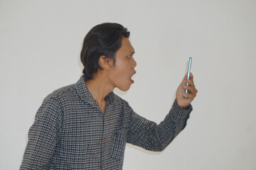 Young Asian man wearing black shirt surprised while looking at smartphone isolated on white background